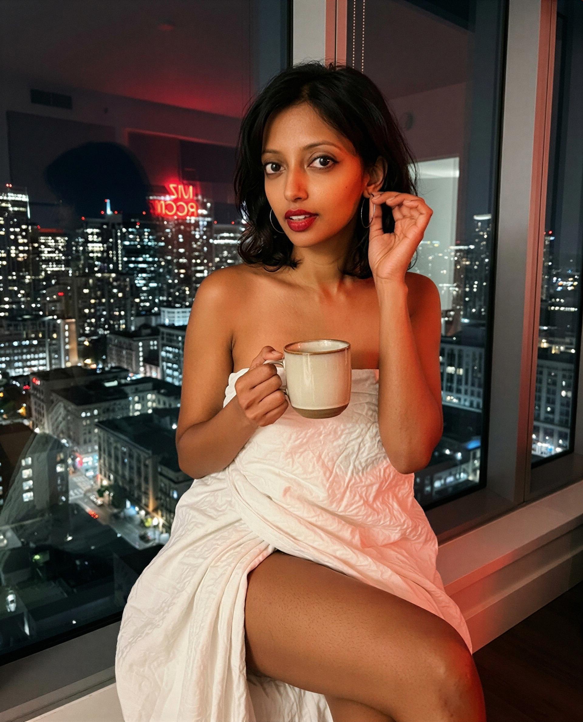 Wrapped in sheets, city lights, and a warm cup - want to see if I’m even better up close? 😘, by Uma Iyengar